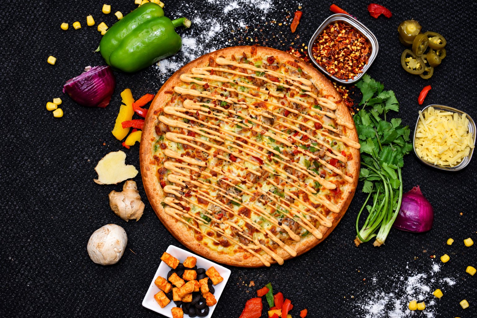 A Bee Pizzeria pizza with a criss-cross sauce drizzle, surrounded by fresh capsicum, chilli and herbs